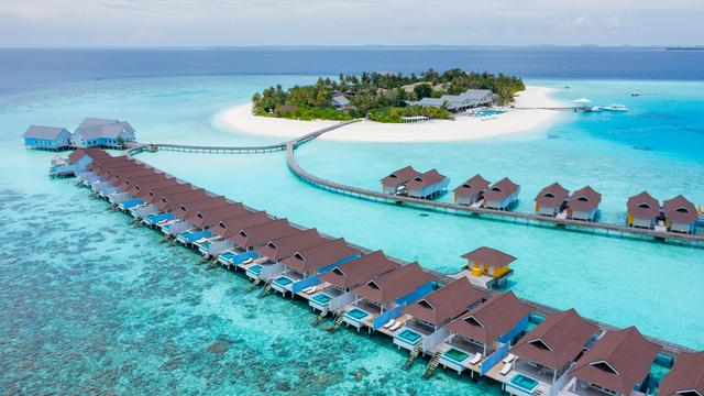 Overwater Maldives pool villas beside a white-sand island and crystal-clear lagoon.