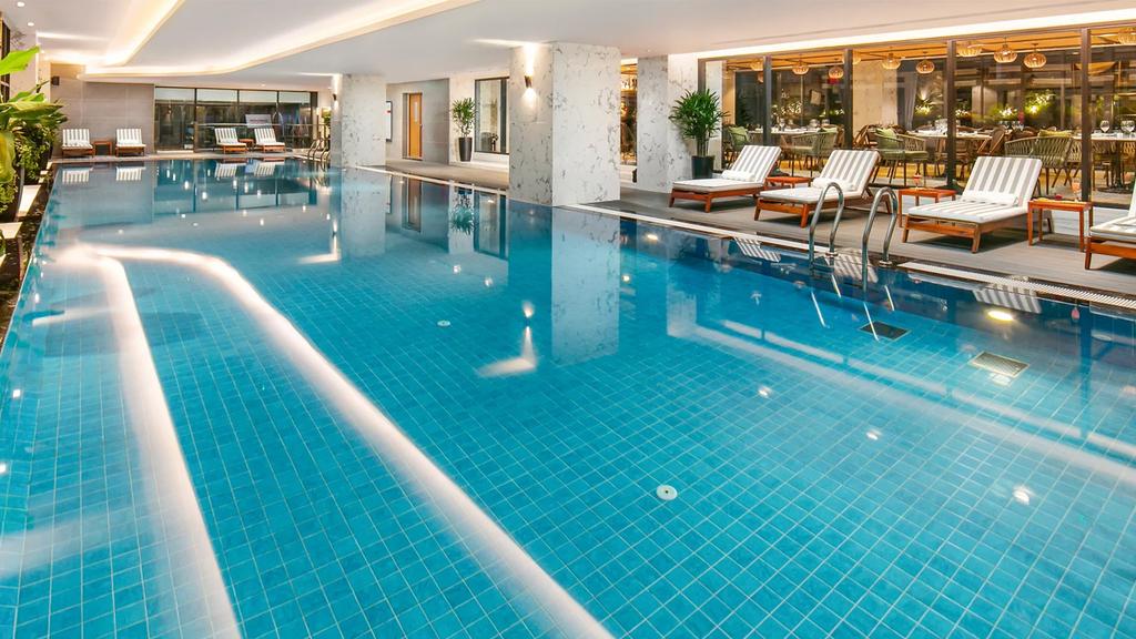 Indoor saltwater pool at Mövenpick Hanoi with deck chairs and restaurant view.