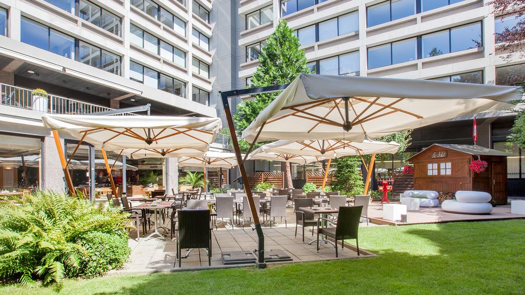 Outdoor dining area at Crown Plaza Geneva with umbrellas and garden seating.