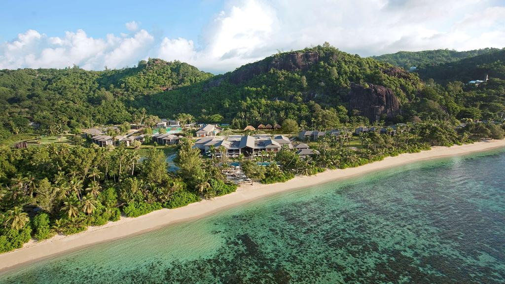 Aerial view of luxury beachfront resort with lush greenery and azure waters.