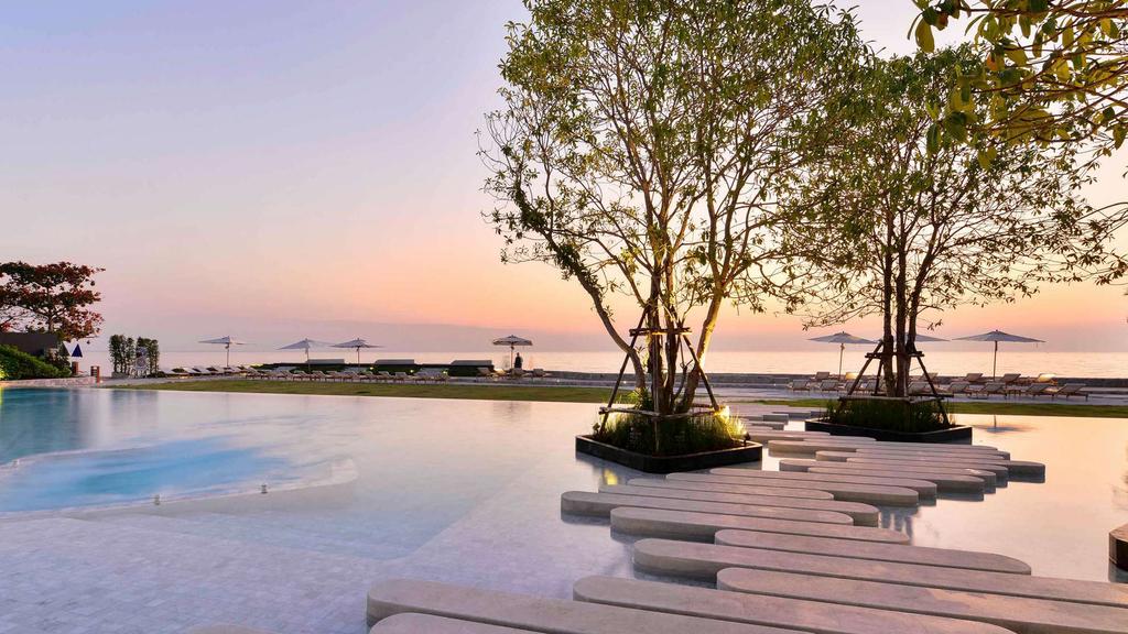 Oceanfront resort pool at sunset with trees and umbrellas.