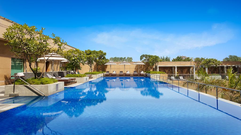 Luxurious outdoor pool at Crown Plaza Gurgaon, surrounded by greenery.