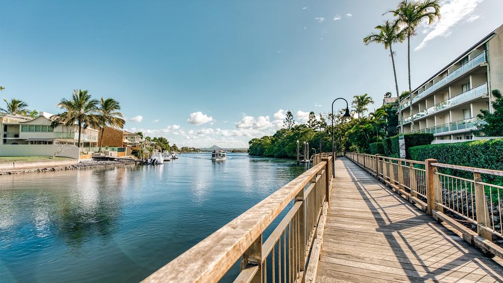 Wooden boardwalk along the water in Noosa with palm trees and buildings.