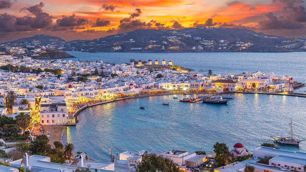 Sunset view over Mykonos harbour with white Cycladic buildings.