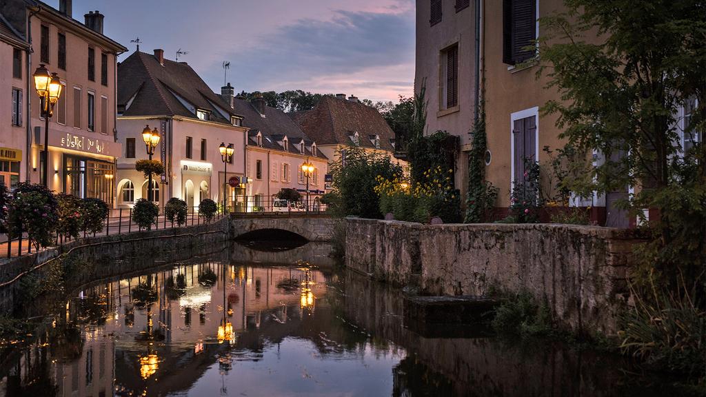 Charming French village with canals and illuminated buildings at dusk.