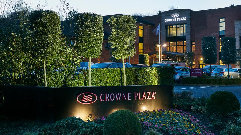 Entrance of Crowne Plaza Belfast surrounded by lush greenery.