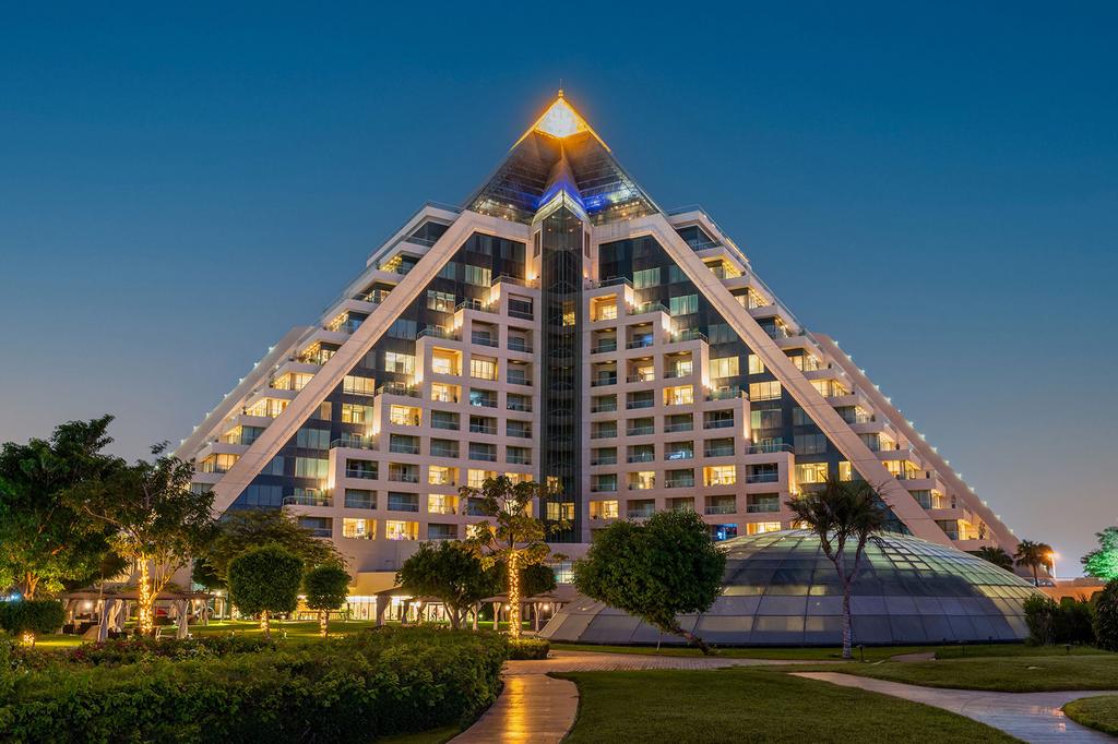 Pyramid-inspired luxury Raffles Dubai hotel with illuminated facade at dusk. 