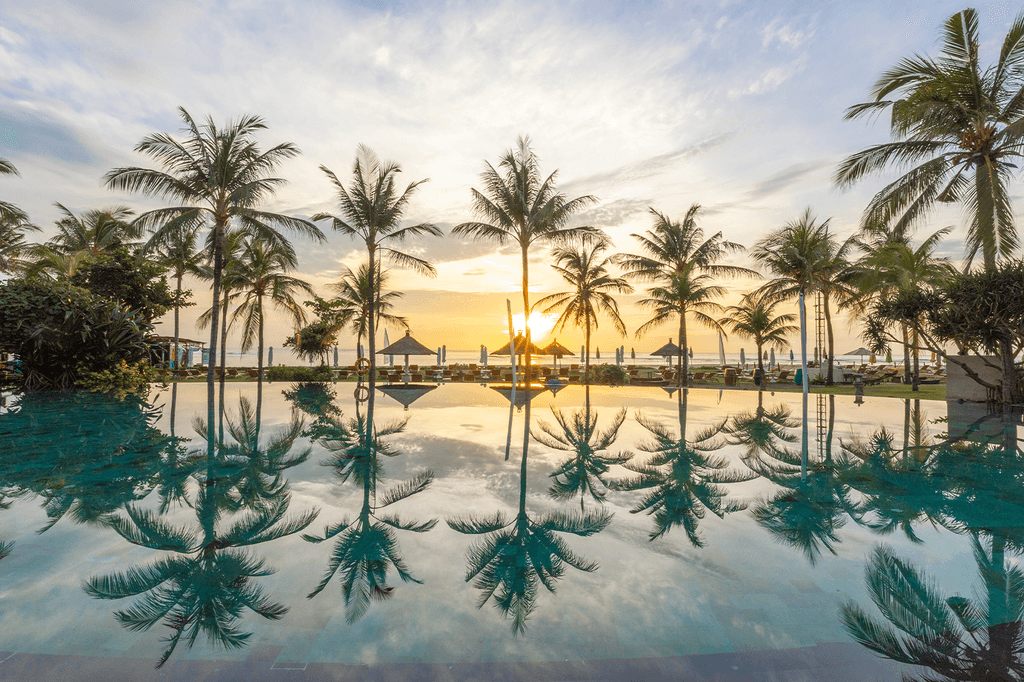 Sunset view at the pool with palm trees in Nusa Dua, Bali.