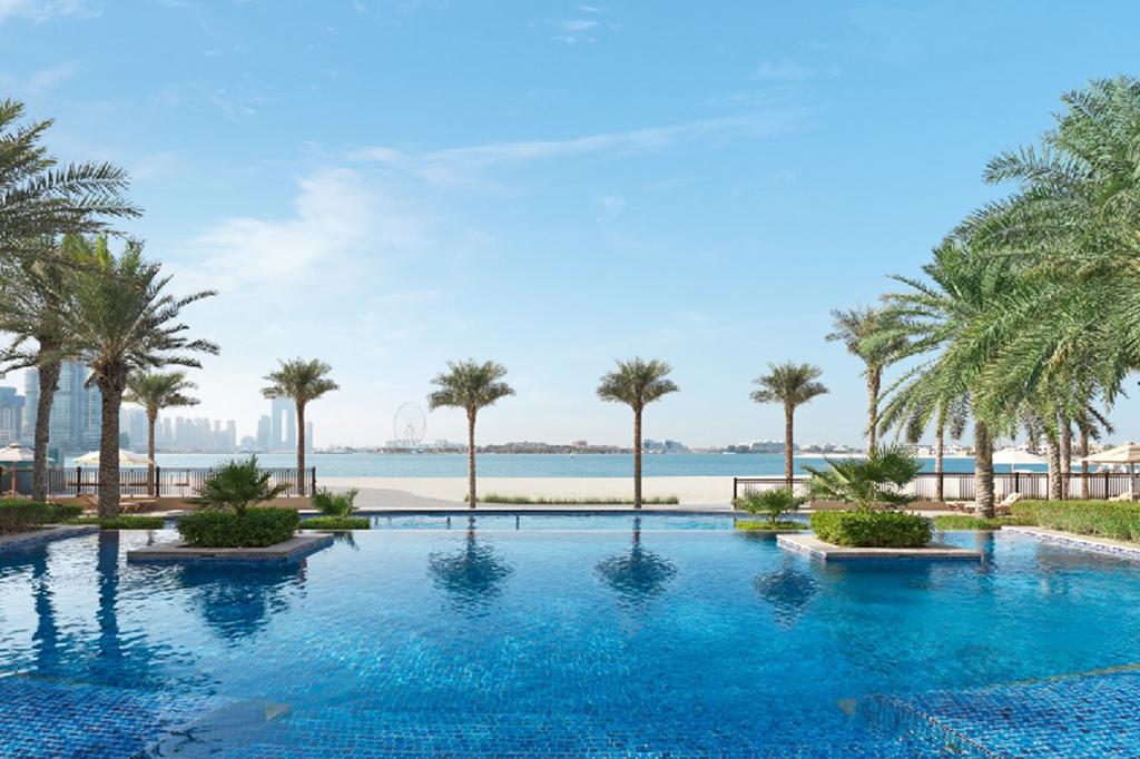 Luxurious pool view at Fairmont Palm Jumeirah, Dubai with palm trees and sea.