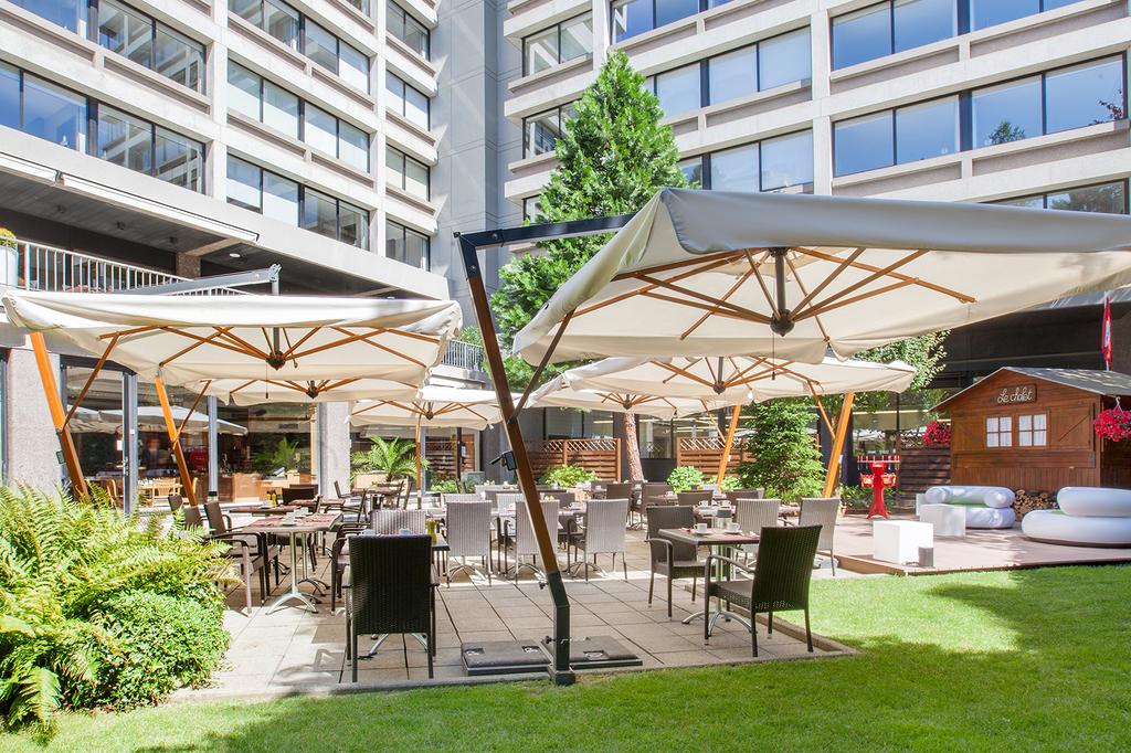 Outdoor dining area at Crown Plaza Geneva with umbrellas and garden seating.