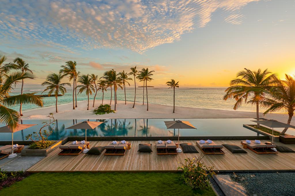 Scenic Maldives island resort with palm trees and beachfront infinity pool at sunset.