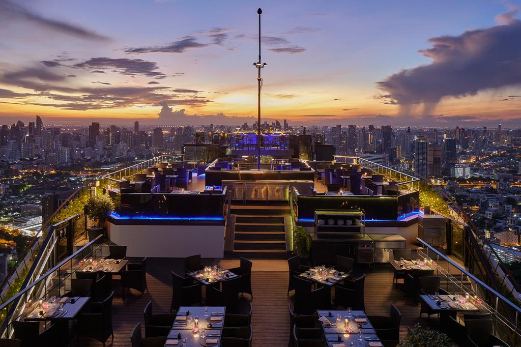 Rooftop bar overlooking Bangkok's skyline at sunset.