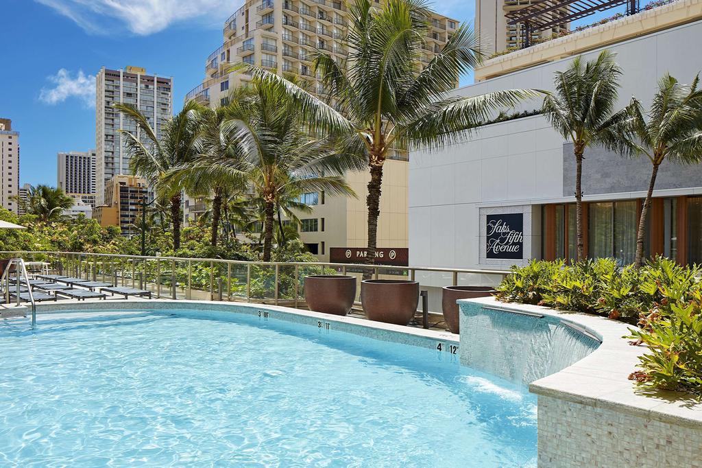 A stylish Waikiki hotel pool area with city and palm tree views.