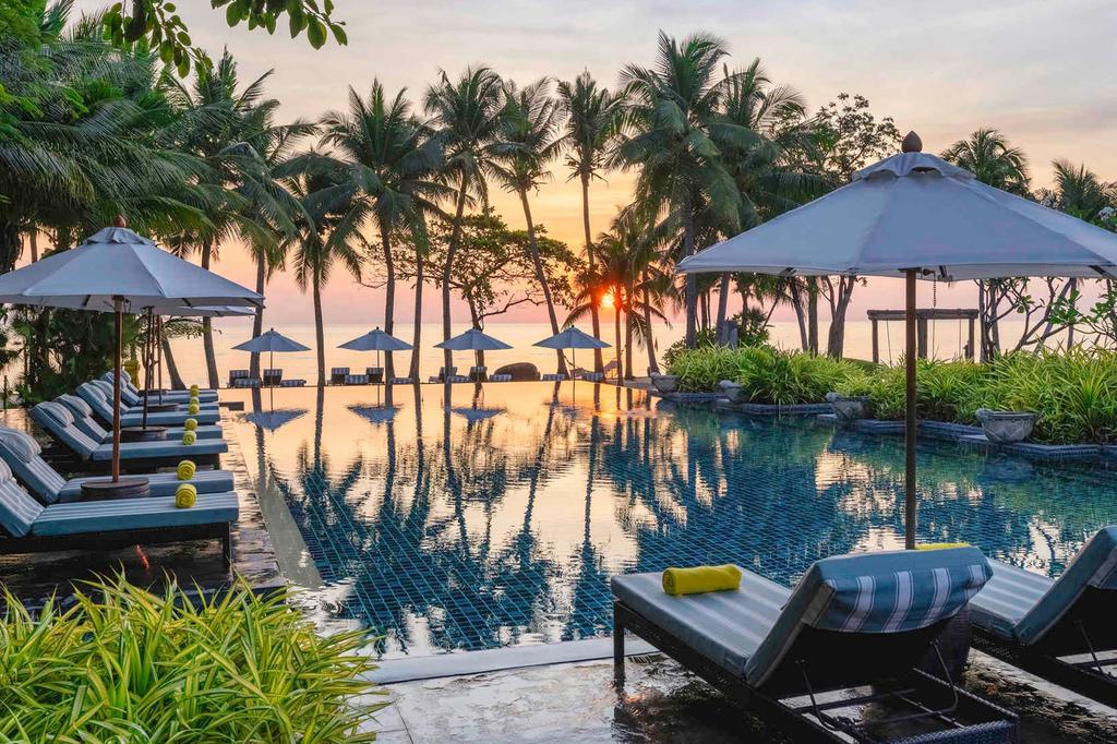 Serene poolside at a tropical beachfront resort during sunset.