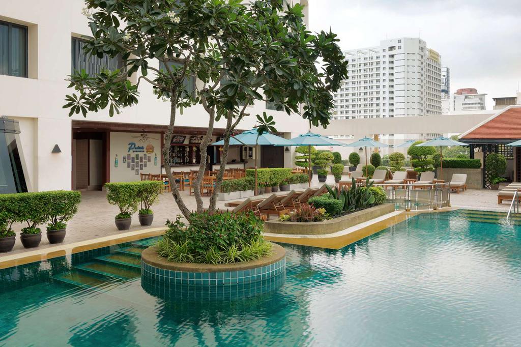 Rooftop pool with sun loungers and greenery at a Bangkok hotel.