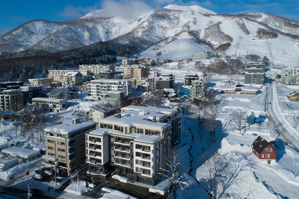 Snow-covered Hirafu Village with modern buildings and mountain backdrop.