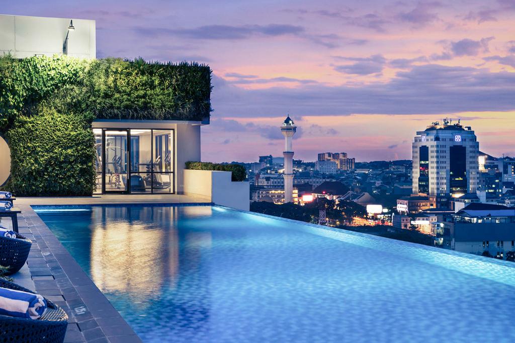 Rooftop pool with city skyline view at sunset in Bandung hotel.