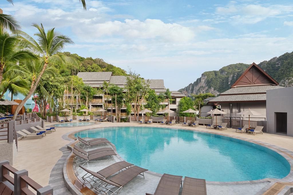 Tropical resort pool surrounded by lush greenery and mountains.