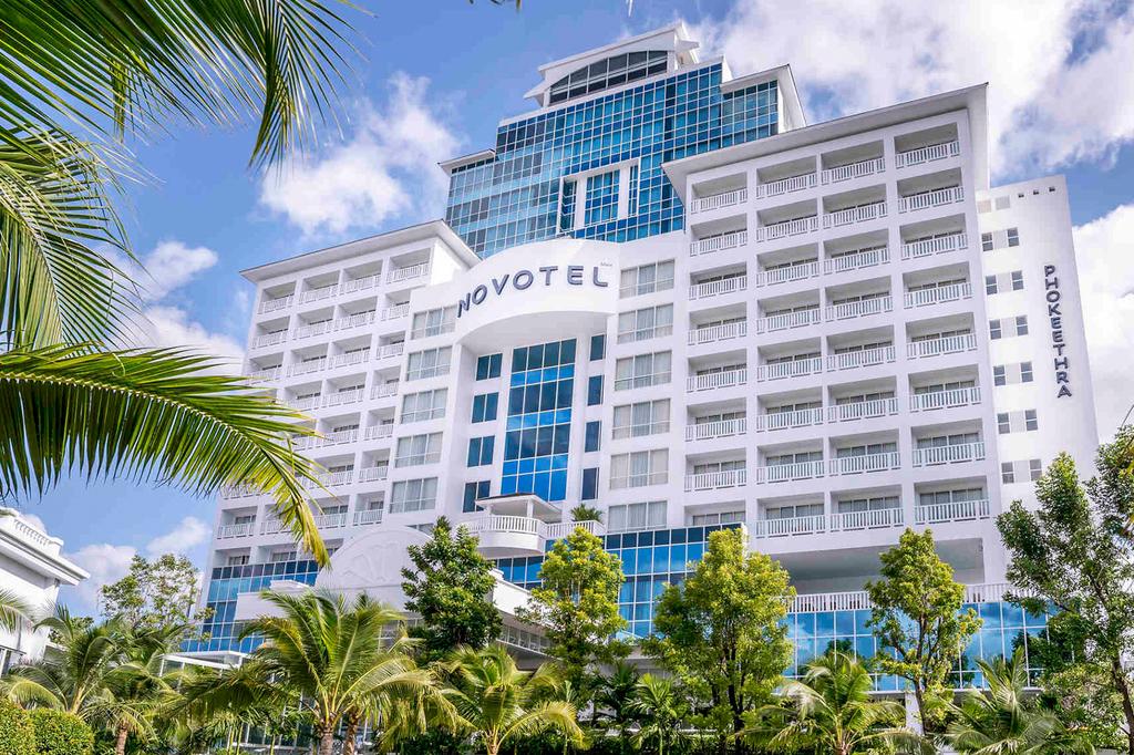 Modern hotel in Phuket surrounded by palm trees under a clear sky.