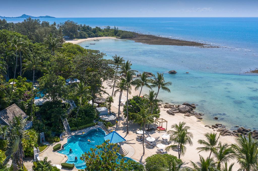 Aerial view of a beachfront resort with lush gardens and clear blue waters.