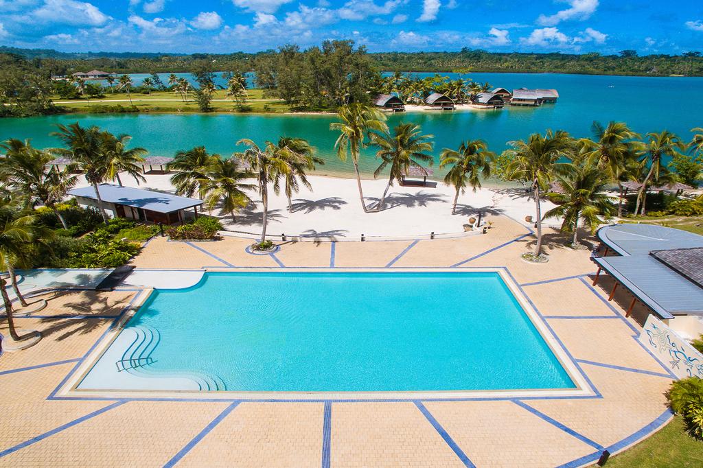 A tropical resort with a large pool overlooking a turquoise lagoon.