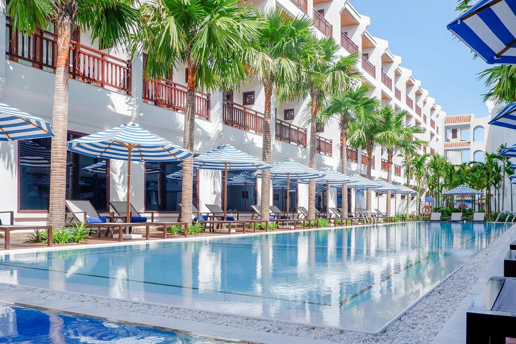 Luxurious Wafaifo Resort Hoi An pool with sun loungers and palm trees. 