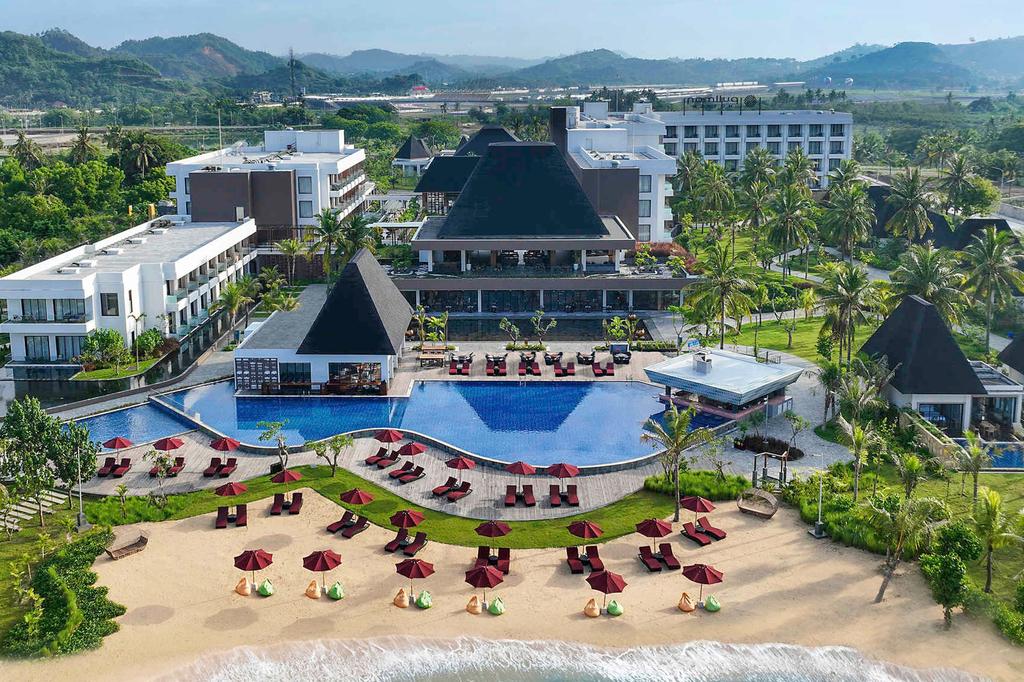 Beachfront resort with pool and sun loungers on sandy beach.