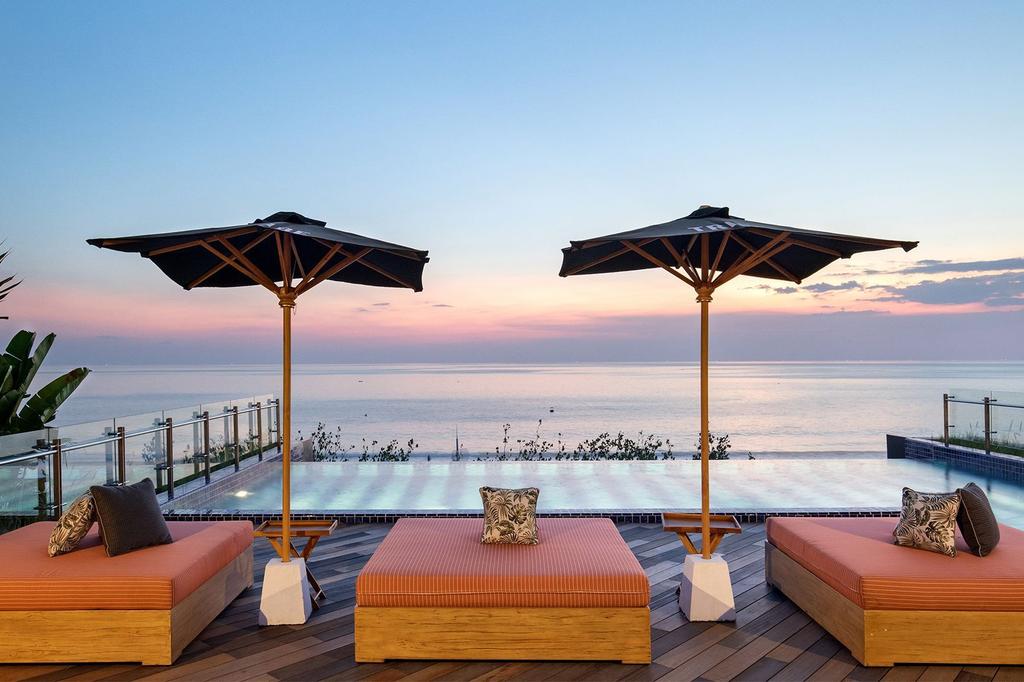 Beachfront infinity pool at sunset with lounge beds and umbrellas.