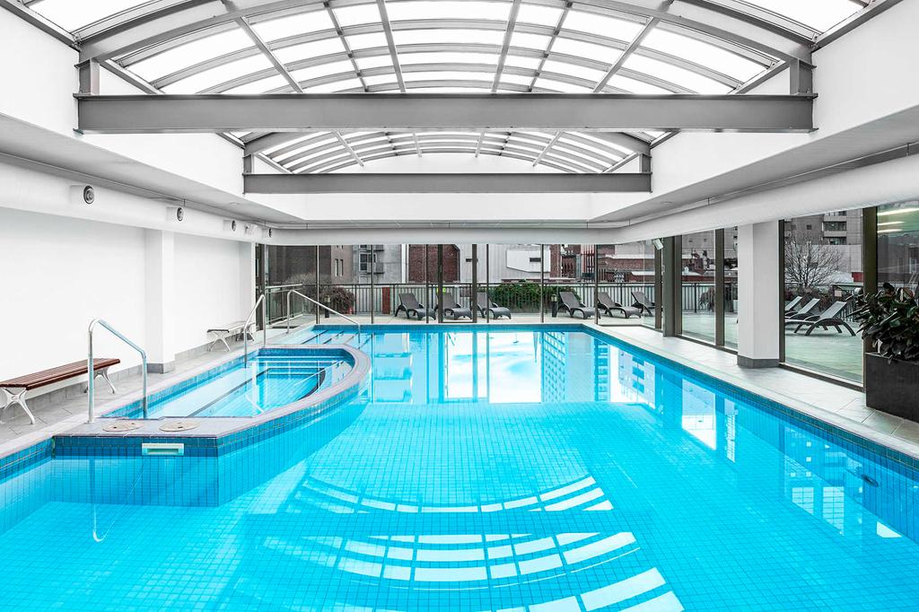 Indoor heated pool with spa at a Melbourne hotel under glass ceiling.