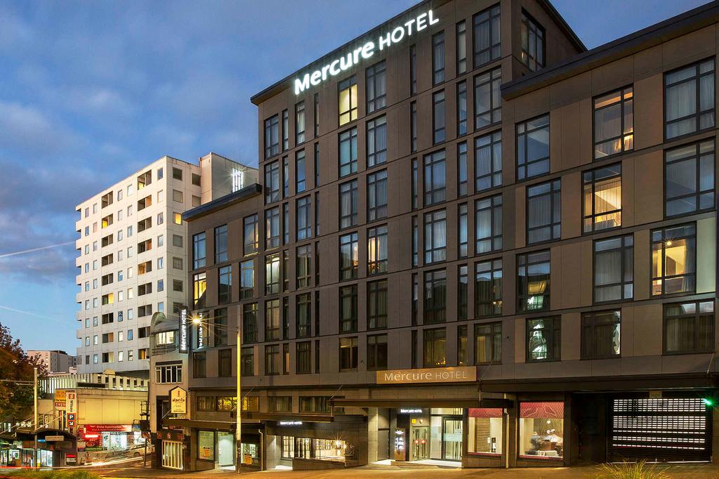 Modern hotel in Auckland CBD with illuminated exterior at dusk.