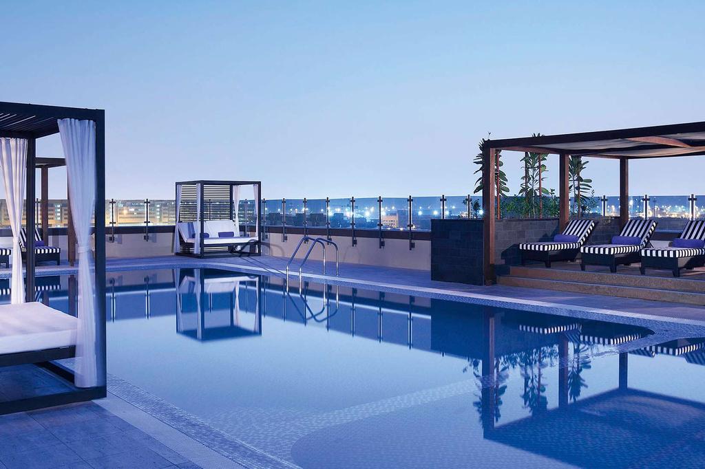 Chic rooftop pool lounge at Dubai Pullman with city views.