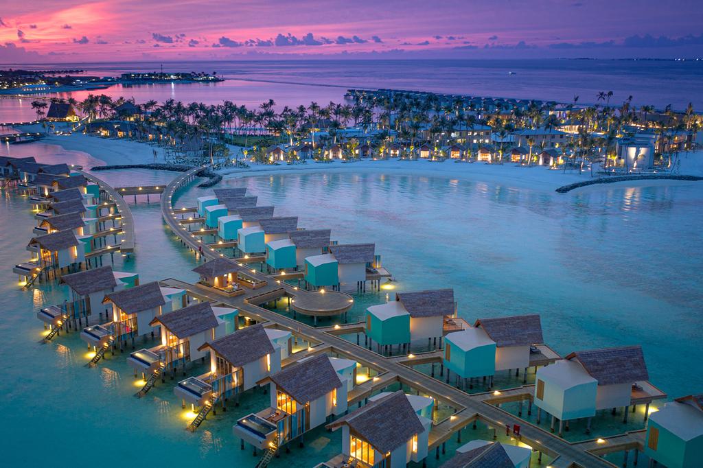 Aerial view of Hard Rock Maldives' overwater bungalows at sunset.  