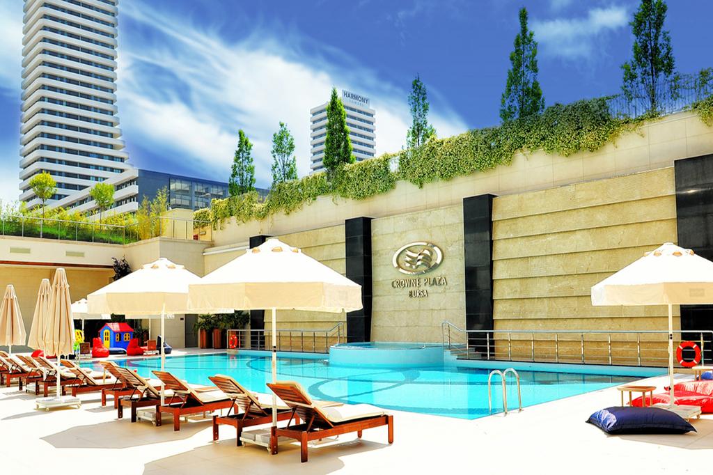 Outdoor pool area at Crowne Plaza Bursa with modern buildings in the background.